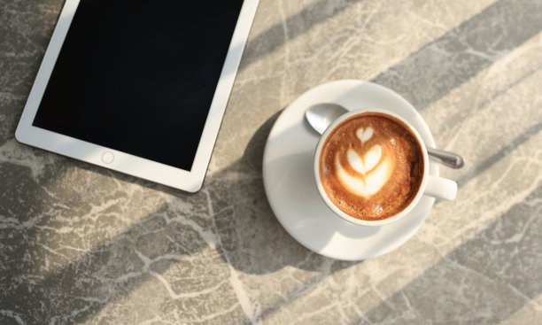 木桌上数码平板电脑旁的白色热咖啡杯。简单的工作空间或早上的咖啡休息时间/选择性专注图片下载