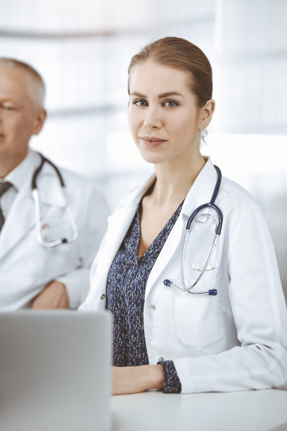 在阳光明媚的诊所里，老年医生和他的女同事坐在工作地点讨论目前的疾病治疗。医学中的团队合作图片下载