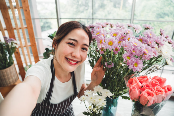 在花店里，年轻的花商与花瓶里漂亮的鲜花自拍。图片下载