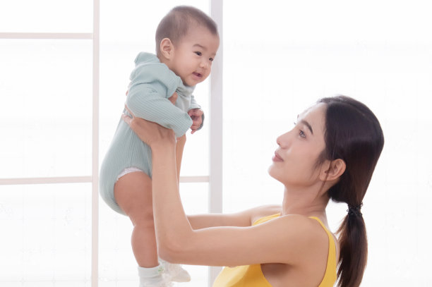 美丽的亚洲母亲在空中抱着婴儿，在家里玩耍时带着爱和温柔看着婴儿。小孩子和妈妈在白色房间里玩耍。快乐童年的概念。图片下载
