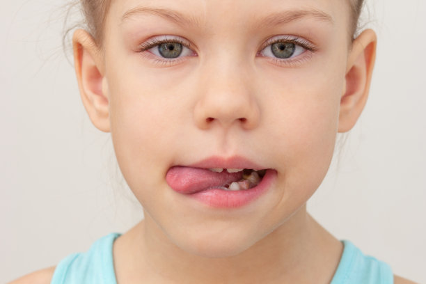 孩子的脸，舌头向左侧伸出，头发剪短，白人小女孩，67岁，灰色背景图片下载