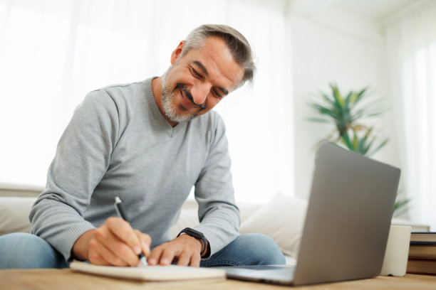 微笑成熟的男人写作和使用笔记本电脑图片下载