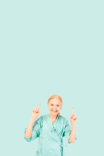 微笑的老年病人妇女穿着病人制服看着相机老太太指着上面的医疗保健医院和保险概念隔离在绿色背景复制空间图片下载