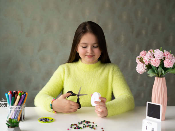 一个长头发、穿黄色毛衣的小女孩编织着串珠首饰图片下载