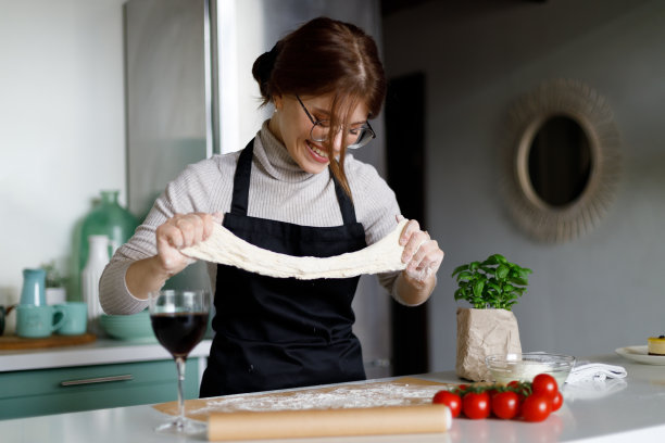 微笑的年轻家庭主妇在厨房里伸展披萨面团。图片下载
