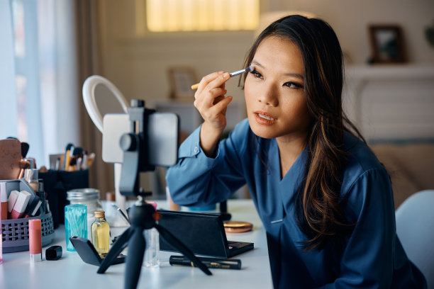 年轻的亚洲女性在家里化妆时看着智能手机屏幕。图片下载