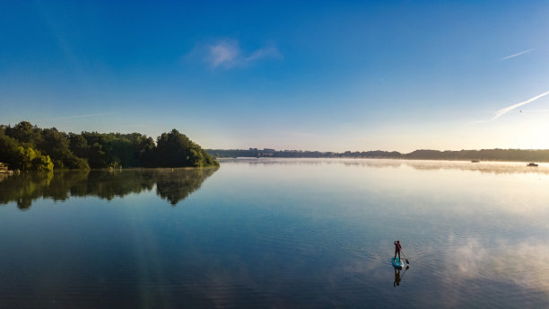 在日落或日出时，女子在美丽的湖上划桨，站着划桨在德国梅克伦堡湖区冒险图片下载