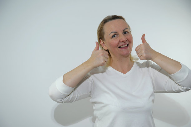 微笑的年轻红发身材积极的女性女孩20多岁，穿着白色空白设计的休闲t恤，在黄色背景的工作室肖像上摆出大拇指向上看的姿势图片下载