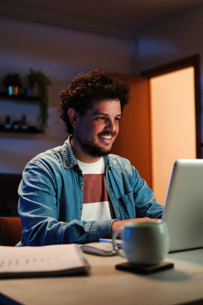 垂直的。快乐的自由职业者在家里工作，晚上把笔记本电脑放在桌子上。年轻人微笑着在客厅用电脑上网。企业家寻求银行融资投资图片下载