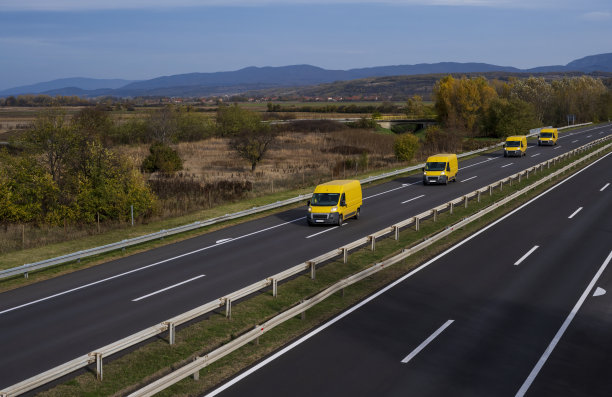 四辆黄色现代快递小件货物快递车在高速公路上快速行驶到市区郊区。在高速公路上排成一列的小型货车车队。黄色的小货车。图片下载