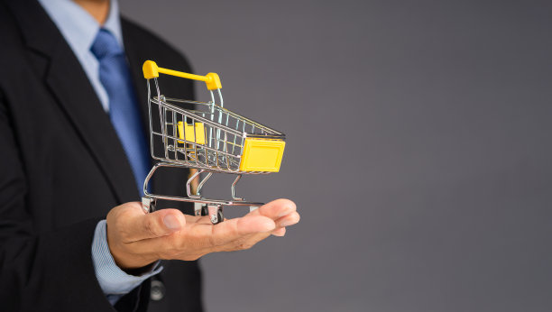 商人在灰色背景上展示一个迷你购物车。图片下载
