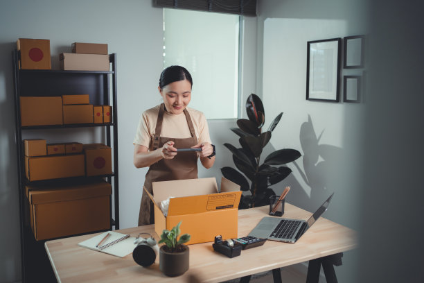 亚洲女卖家在打包货物准备发货前用智能手机拍照。图片下载