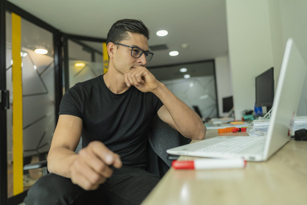 一个拉丁裔男子在他工作的公司的办公室里，拿着一台笔记本电脑整理待处理的工作图片下载