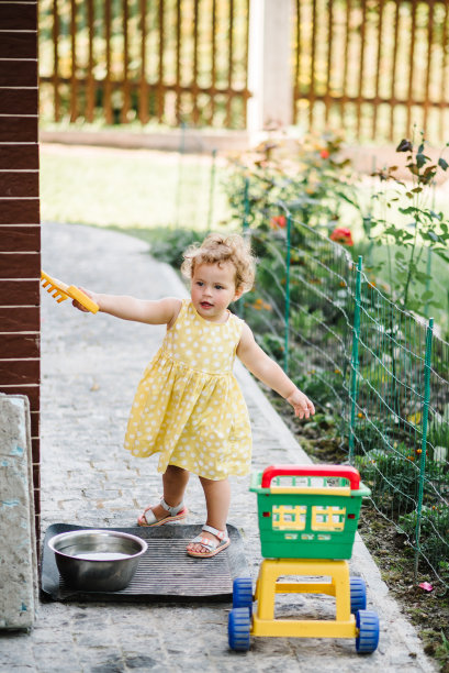 一个小女孩在后院玩手推车。孩子拿着玩具卡车。早年学习快乐童年的概念。图片下载