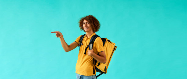 一个穿着黄色制服、背着黄色快递背包的英俊年轻人指着旁边，站在蓝色背景下微笑着。图片下载