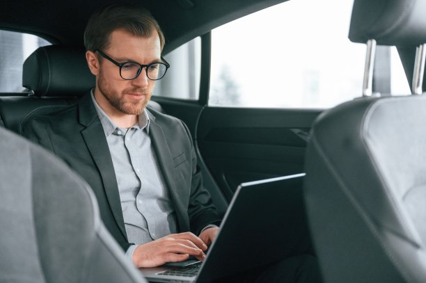 戴着眼镜，用笔记本电脑工作。穿着正式职业装的男人坐在现代汽车里图片下载