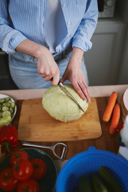 一名妇女在木板上用刀切卷心菜。一位女士正在准备健康的蔬菜沙拉图片下载