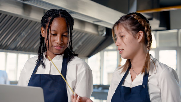 非洲女孩手里拿着笔记本电脑，另一个女性朋友手里拿着一杯意大利面。还有其他配料，比如鸡蛋。谈谈你手里的杯子里的意大利面。图片下载