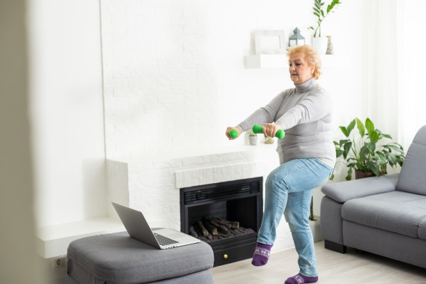 在家训练。运动资深女性做瑜伽平板支撑，同时在笔记本电脑上观看在线教程，在客厅锻炼，自由空间，全景图片下载