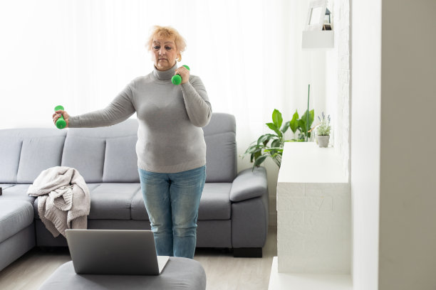 家里的运动。活跃的老年妇女做热身伸展运动在笔记本电脑前，训练与在线教程图片下载