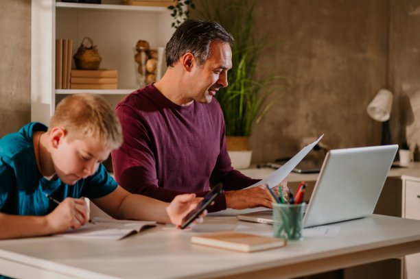 忙碌的父亲在用笔记本电脑工作，而儿子在用智能手机。图片下载