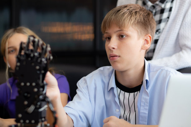 白人两个十几岁的学生在学校一起在教室里学习机械臂，男孩和女孩用控制器学习机器人AI与老师的认知、教育和发展理念。图片下载