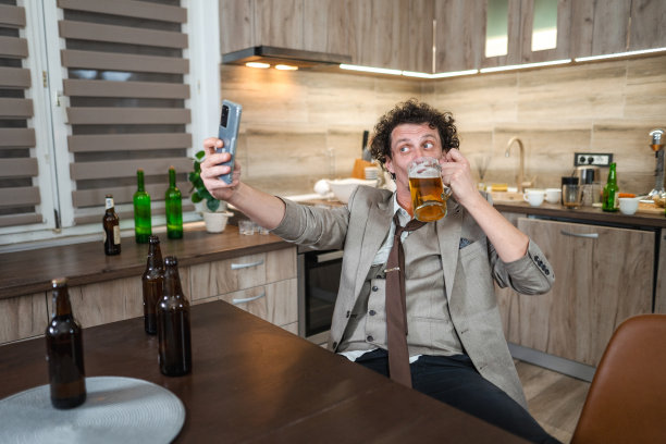 微笑的醉汉拿着一杯啤酒自拍，周围都是空啤酒瓶图片下载