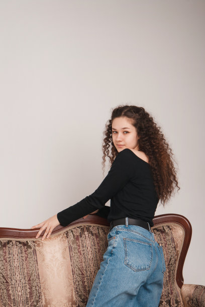 时尚女性肖像。微笑的卷发黑发女孩在白色背景上对着相机摆出美丽的姿势。图片下载