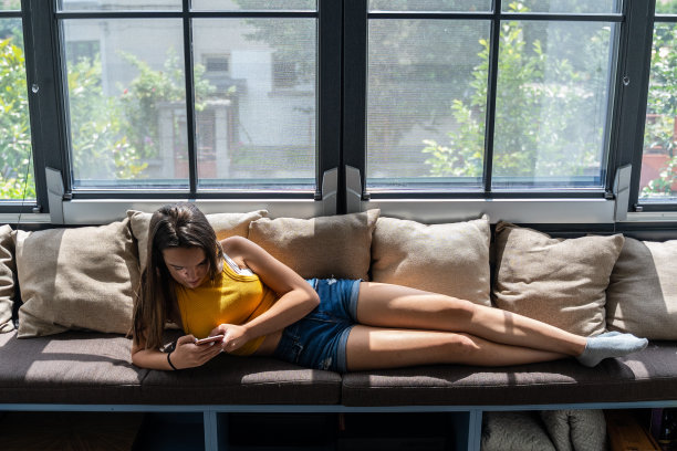 拿着手机的少女在沙发上放松。图片下载