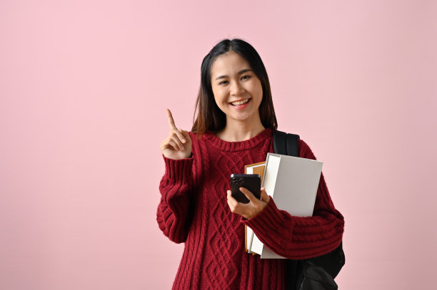 快乐的亚洲女大学生拿着课本，手指朝上图片下载