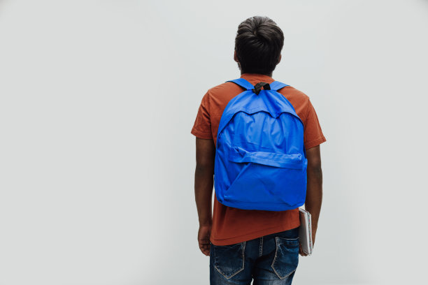 印度学生背着蓝色背包，戴着眼镜，拿着笔记本，在灰色背景上摆姿势。教育和学校教育的概念。是时候回学校了图片下载