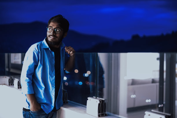 一个戴着眼镜，穿着蓝色衬衫的印度人在晚上环顾城市。在城市夜晚街道的背景下图片下载