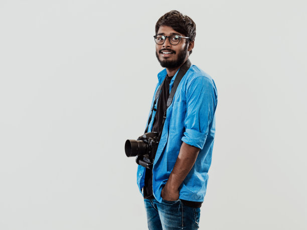 专业摄影师用数码单反相机拍照。印度男子摄影爱好者站在蓝色背景上拍照。影棚拍摄图片下载