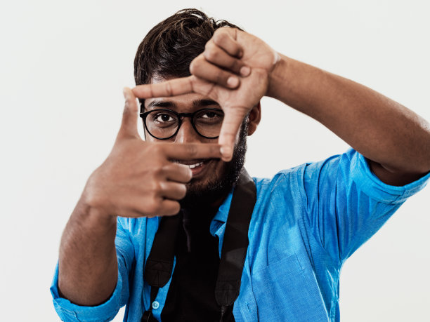 年轻英俊的男子用手指聚焦，在灰色的背景上用双手分开。特写肖像图片下载