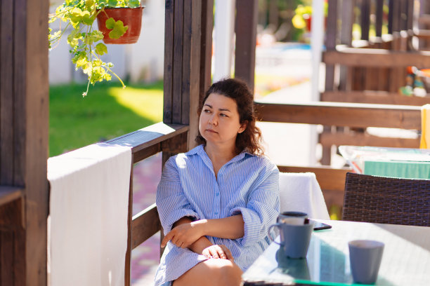 深色头发的中年女人在房子的阳台上喝咖啡。图片下载