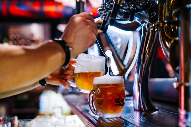 酒吧里，男酒保手握啤酒龙头，用玻璃杯倒啤酒图片下载