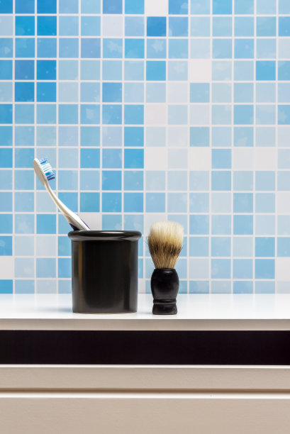 一个胡须皂刷和一个装牙刷的容器，放在白色的浴室柜上图片下载