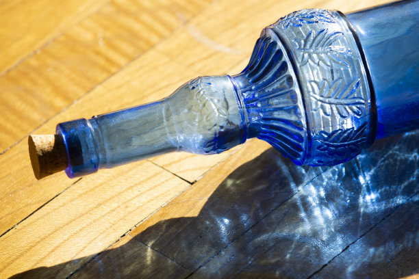 一个蓝色的装饰玻璃瓶，放在橡木表面，被早晨的一缕阳光刺穿图片下载