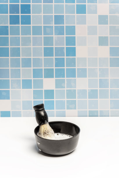 在一间铺着蓝色瓷砖的浴室里，白色的表面上涂着肥皂的碗里的理发刷图片下载