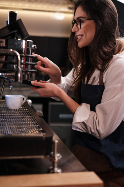 一位快乐的女服务员在自助餐厅的浓缩咖啡机上煮着新鲜的咖啡。图片下载