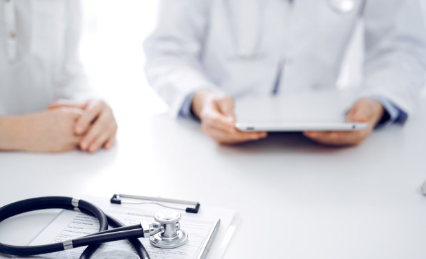 听诊器放在平板电脑上，医生和病人并排坐着，使用平板电脑作为背景。医学、保健理念图片下载