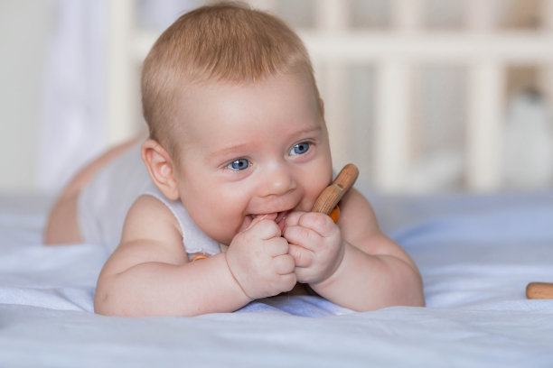 一个可爱的男孩在明亮的卧室里。一个刚出生的婴儿躺在床上啃玩具。牙齿在长牙。婴儿的牙龈发痒。一个孩子看着镜头。家庭、怀孕和分娩。图片下载