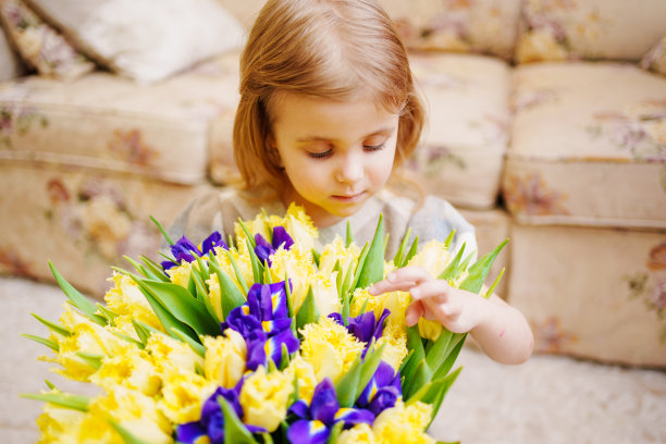 一个可爱的小女孩拿着一束黄色郁金香和紫色鸢尾花的肖像图片下载