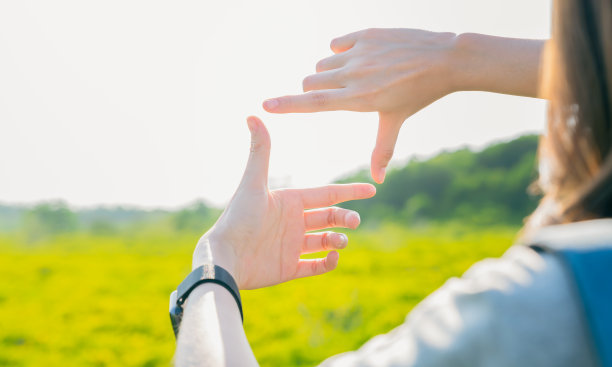手工制作的画框手势与在春天花园的背景下看树上早午餐，创意和想象力的概念。图片下载