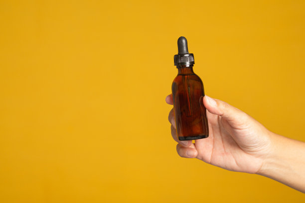 手拿着一个棕色的玻璃瓶，没有黄色背景上的广告标签。图片下载