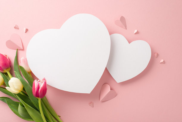 精致的郁金香花朵的俯视图照片，粉红色的纸心在柔和的粉红色背景上，有两个空的心为文字或广告图片下载