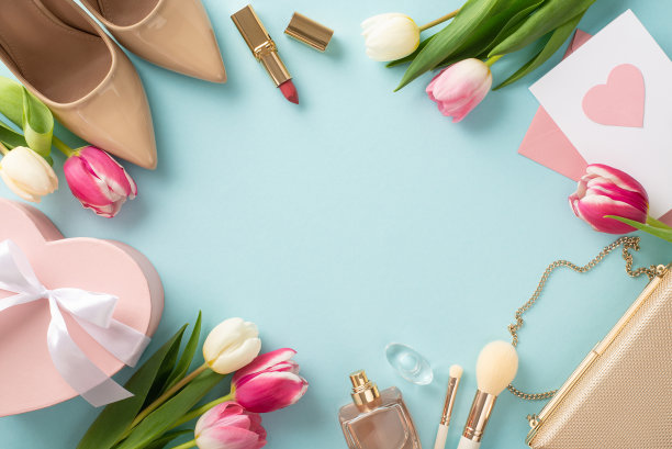 女性母亲节的概念。顶视图平面布局的高跟鞋，手提包，礼品盒，郁金香，口红，化妆刷和耳环在柔和的蓝色背景与空间的文字或广告图片下载