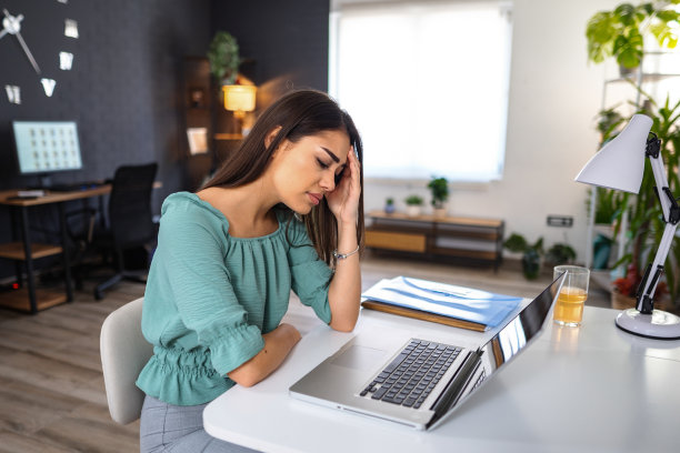 年轻女子在家里用笔记本电脑工作时感到头痛图片下载