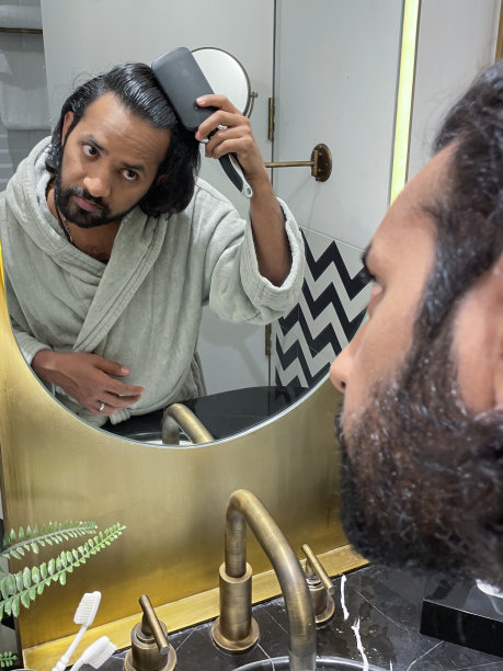 镜子里的特写，印度男人穿着浴袍站在浴室的水池边，用梳子梳理凌乱潮湿的头发，自我护理和修饰的概念图片下载