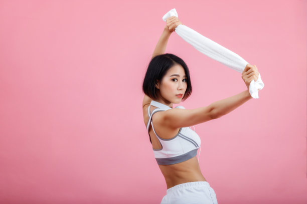 年轻的亚洲妇女，脖子上戴着毛巾和耳机，孤立在粉红色的背景上。健康生活理念。图片下载
